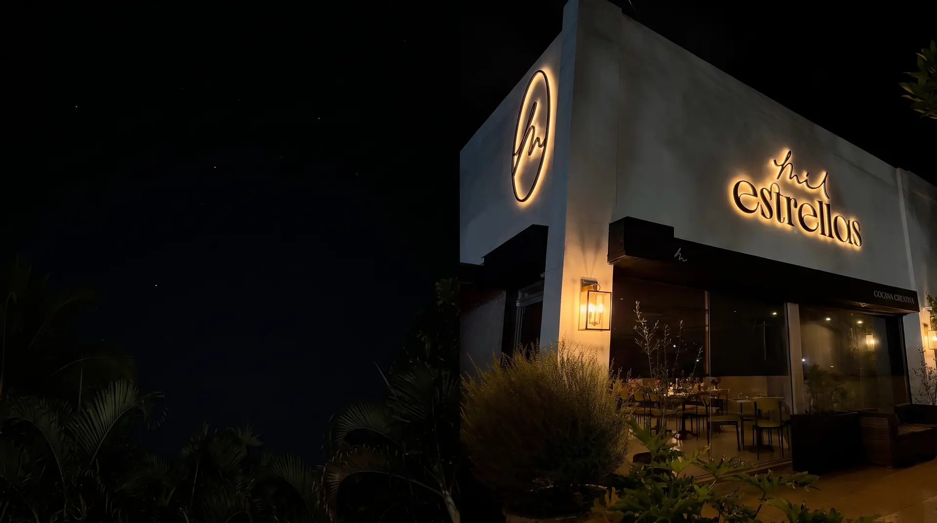 Fachada de Mil Estrellas de noche, con el letrero iluminado y faroles encendidos